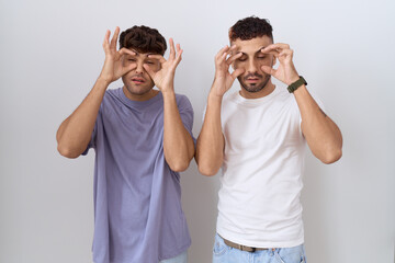 Sticker - Homosexual gay couple standing over white background trying to open eyes with fingers, sleepy and tired for morning fatigue