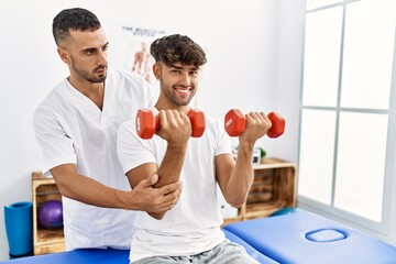 Wall Mural - Two hispanic men physiotherapist and patient having rehab session using dumbbells at clinic