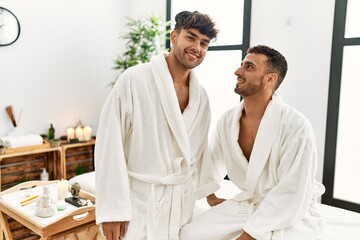 Wall Mural - Two hispanic men couple wearing bathrobe sitting on massage table at beauty center