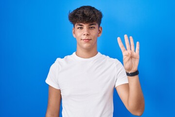 Wall Mural - Hispanic teenager standing over blue background showing and pointing up with fingers number four while smiling confident and happy.