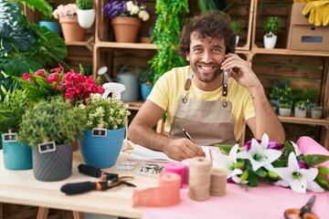 Sticker - Young hispanic man florist talking on smartphone writing on notebook at flower shop