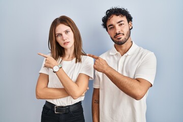 Wall Mural - Young couple wearing casual clothes standing together pointing with hand finger to the side showing advertisement, serious and calm face