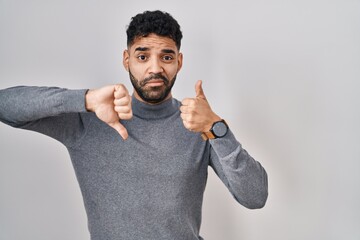 Wall Mural - Hispanic man with beard standing over white background doing thumbs up and down, disagreement and agreement expression. crazy conflict