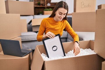 Wall Mural - Young caucasian woman smiling confident unpacking cardboard box at new home