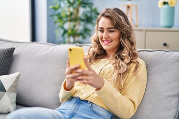 Wall Mural - Young woman using smartphone sitting on sofa at home