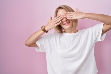 Sticker - Young caucasian woman standing over pink background covering eyes with hands smiling cheerful and funny. blind concept.