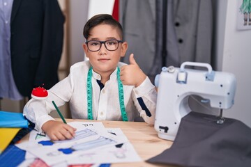 Poster - Young hispanic kid at tailor room smiling happy and positive, thumb up doing excellent and approval sign