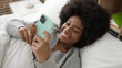 © Krakenimages.com - African american woman using smartphone lying on bed at bedroom