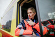 Portrait of young woman doctor sitting and talking in to walkie-talkie in ambulance car.