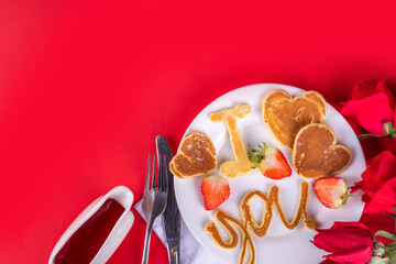 Cute Valentine pancakes, sweet homemade butter cake shaped in form of I love you, Be my heart inscription. Breakfast or gift idea for Saint Valentine day, with strawberry and syrup. on red background