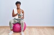 African american woman wearing sportswear sitting on pilates ball pointing aside worried and nervous with forefinger, concerned and surprised expression