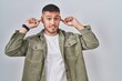 © Krakenimages.com - Young hispanic man standing over isolated background smiling pulling ears with fingers, funny gesture. audition problem
