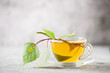 © murziknata - Glass cup of hot, fragrant birch tea on a grey background and a branch of birch leaves