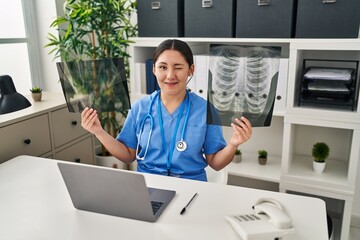 Canvas Print - Young latin doctor woman holding x-ray winking looking at the camera with sexy expression, cheerful and happy face.