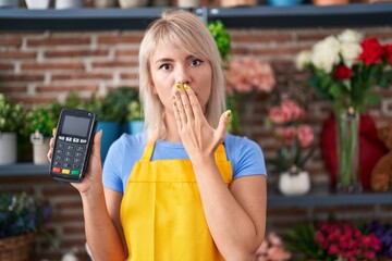 Poster - Young caucasian woman working at florist shop holding dataphone covering mouth with hand, shocked and afraid for mistake. surprised expression