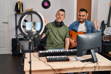 Canvas Print - Two men playing classic guitar at music studio recording song screaming proud, celebrating victory and success very excited with raised arm