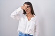 © Krakenimages.com - Young brunette woman wearing glasses peeking in shock covering face and eyes with hand, looking through fingers with embarrassed expression.