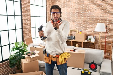 Wall Mural - Handsome middle age man holding screwdriver at new home looking at the camera blowing a kiss with hand on air being lovely and sexy. love expression.