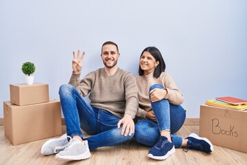 Poster - Young couple moving to a new home showing and pointing up with fingers number three while smiling confident and happy.