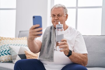 Poster - Middle age grey-haired man make selfie by smartphone holding bottle of water at home