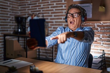 Sticker - Middle age hispanic man using touchpad sitting on the table at night pointing with finger surprised ahead, open mouth amazed expression, something on the front