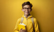© masdika - smiling school kids with eyeglass hold on book in yellow plain background with Generative AI