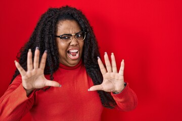 Sticker - Plus size hispanic woman standing over red background afraid and terrified with fear expression stop gesture with hands, shouting in shock. panic concept.