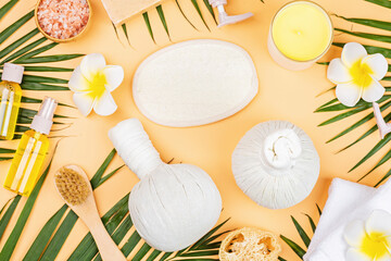 Wall Mural - Spa massage Aromatherapy body care background. Spa herbal balls, cosmetics, towel and tropical leaves on orange table. Top view, flat lay, overhead, copy space. Beauty and health care concept