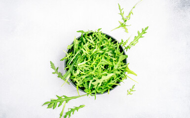 Wall Mural - Fresh green arugula in ceramic bowl on grey kitchen table, top view, copy space. Spring spicy herb for healthy diet eating