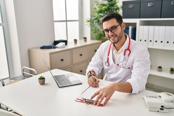 Sticker - Young hispanic man wearing doctor uniform writing report working at clinic