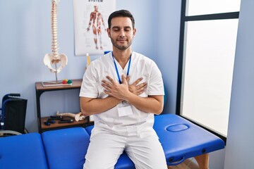 Sticker - Young hispanic man with beard working at pain recovery clinic smiling with hands on chest with closed eyes and grateful gesture on face. health concept.