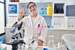 © Krakenimages.com - Hispanic girl with down syndrome working at scientist laboratory showing and pointing up with fingers number three while smiling confident and happy.
