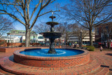 Fototapeta  - A gorgeous winter landscape at the Marietta Square with red brick footpath, a water fountain, bare trees and lush green plants with a clear blue sky in Marietta Georgia USA