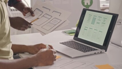 Wall Mural - cropped shot of two male ux designer discussing scheme of mobile app interface on paper and laptop a