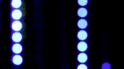 Wall Mural - Vertically falling blue blurry dots. Blue bokeh with reflexes fall down on a black background. Defocused circle lights in rows. Loop 4K video.