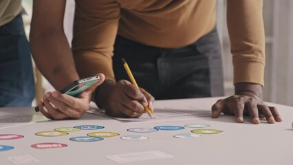 Wall Mural - Cropped shot of team of mobile app developers holding smartphone and making notes on sketches while working on UX design project at office table