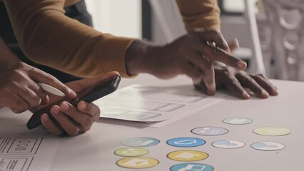 Wall Mural - Close up shot of mobile app developers using smartphone and making notes on sketches while working together on UX project in office