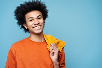 Wall Mural - Closeup portrait of smiling African American man wearing stylish clothes isolated on blue background, copy space. Happy smart student with curly hair looking at camera posing for pictures, studio shot