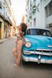 © Daniel Gonzalez/Stocksy - Cuban woman touching hair near vintage car