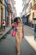 © Daniel Gonzalez/Stocksy - Happy Cuban female touching hair and walking on street