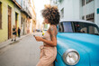 © Daniel Gonzalez/Stocksy - Cuban woman using smartphone near car