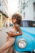 © Daniel Gonzalez/Stocksy - Cheerful Cuban woman with smartphone leaning on car