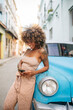 © Daniel Gonzalez/Stocksy - Cuban female using cellphone and leaning on car