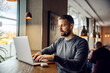 © Dusan Petkovic - A freelancer is sitting at cafeteria and typing report on a laptop while working remotely.