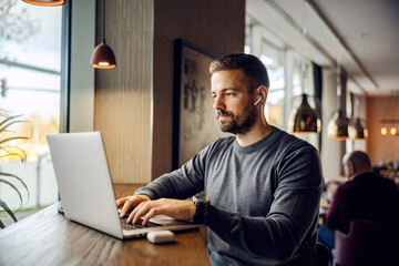 a freelancer is sitting at cafeteria and typing report on a laptop while working remotely.