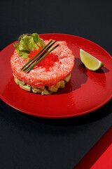 Wall Mural - Tartar with salmon and caviar with lime at red color plate at black and red background with sunlight and shadows, minimalism,top view.