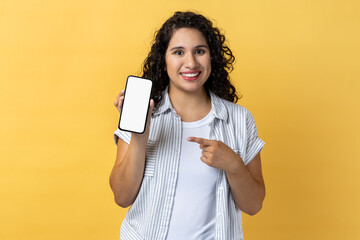 portrait of smiling attractive young adult woman with dark wavy hair holding pointing at cell phone 