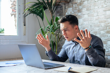 Unhappy young caucasian male worker in glasses look at laptop screen shocked by gadget breakdown or operational problems. Frustrated man confused surprised by unexpected error on computer device..