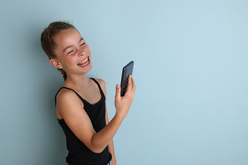 Little emotional teenage girl in pink shirt 11, 12 years old on an isolated blue background with a tablet in her hands.Children's studio portrait. Place the text to copy the place for the inscription