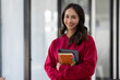 © David - Image of young indian girl asian woman, company worker in dress red shirt, smiling and holding digital tablet, standing over office background